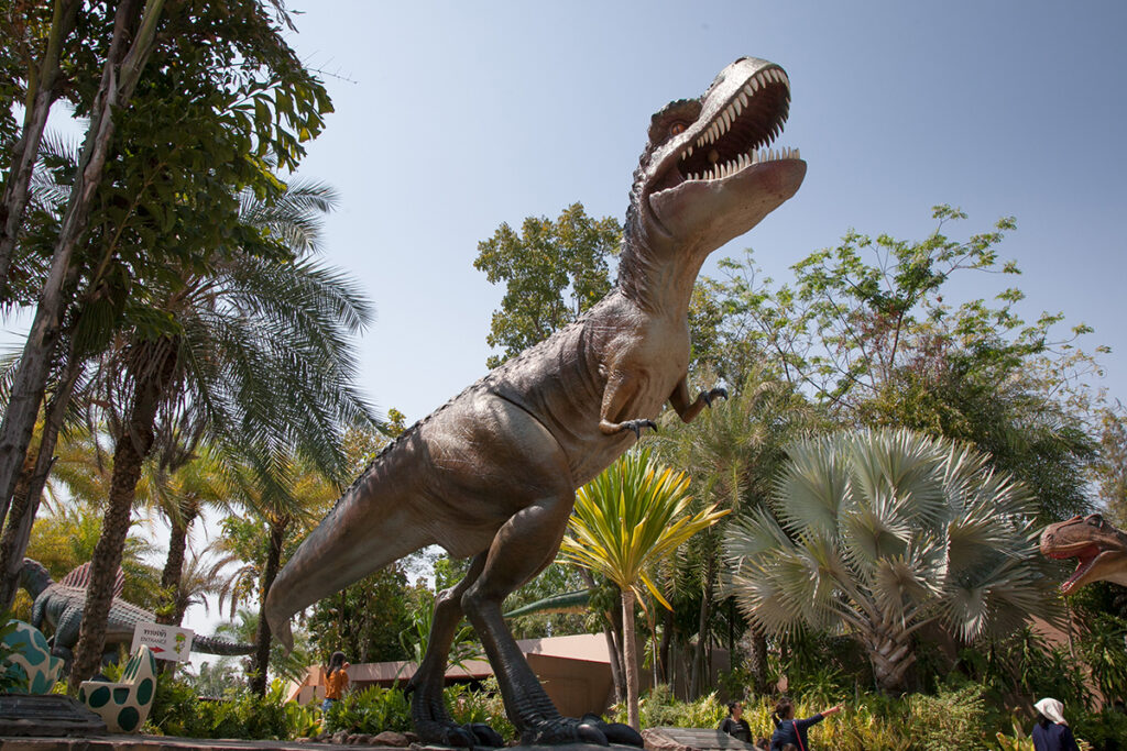 Lifelike Tyrannosaurus rex statue surrounded by tropical foliage at Sirindhorn Dinosaur Museum in Thailand.