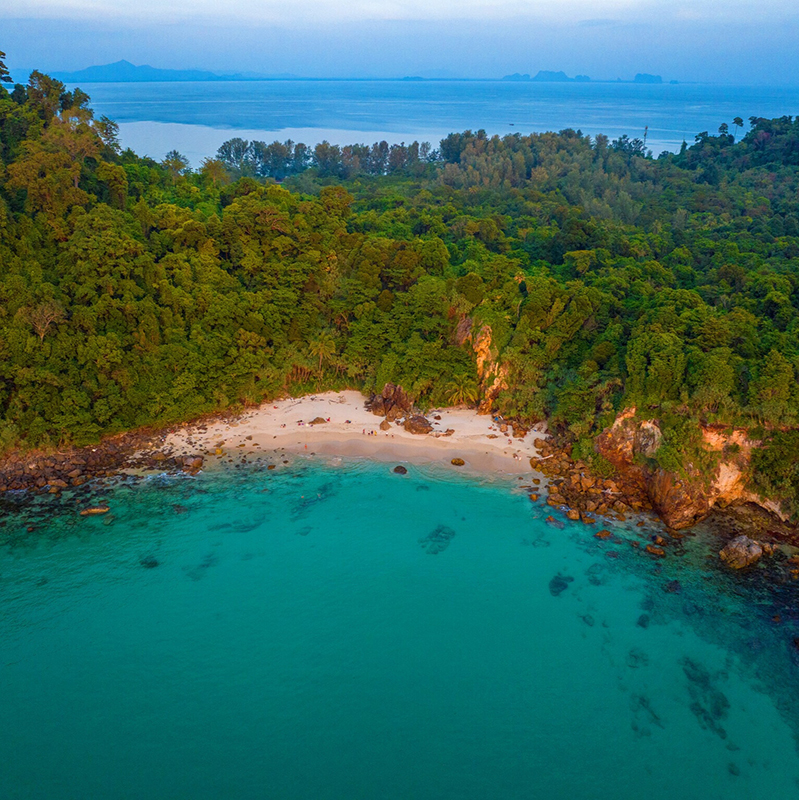 Sunlit view of Sunset Beach, Ko Kradan, with clear turquoise water and white sand under a bright sky