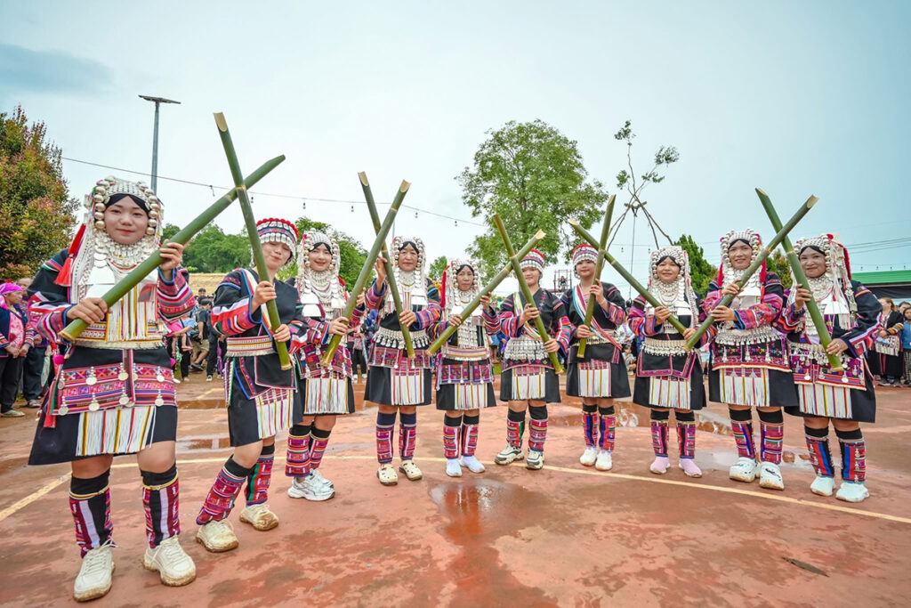 A group of Akha women in traditional dress hold bamboo instruments and pose together at the festival.