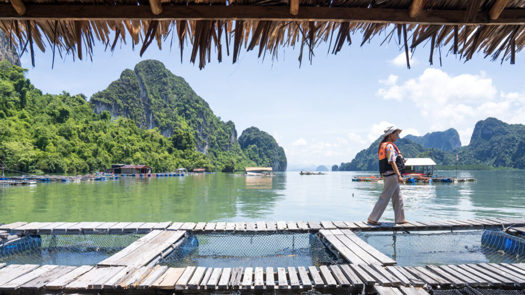 Visitor explores floating fish farm at Ban Laem Sak Community, Krabi, with limestone cliffs and sustainable coastal tourism.