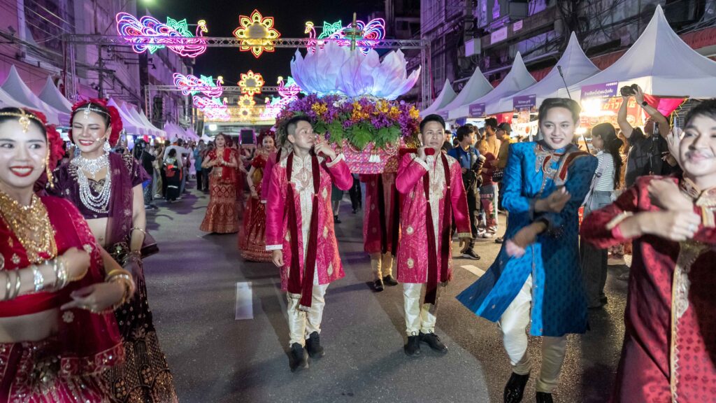 Male and female performers in colorful Indian outfits dance along the illuminated Phahurat Street during the Grand Diwali parade in Bangkok.