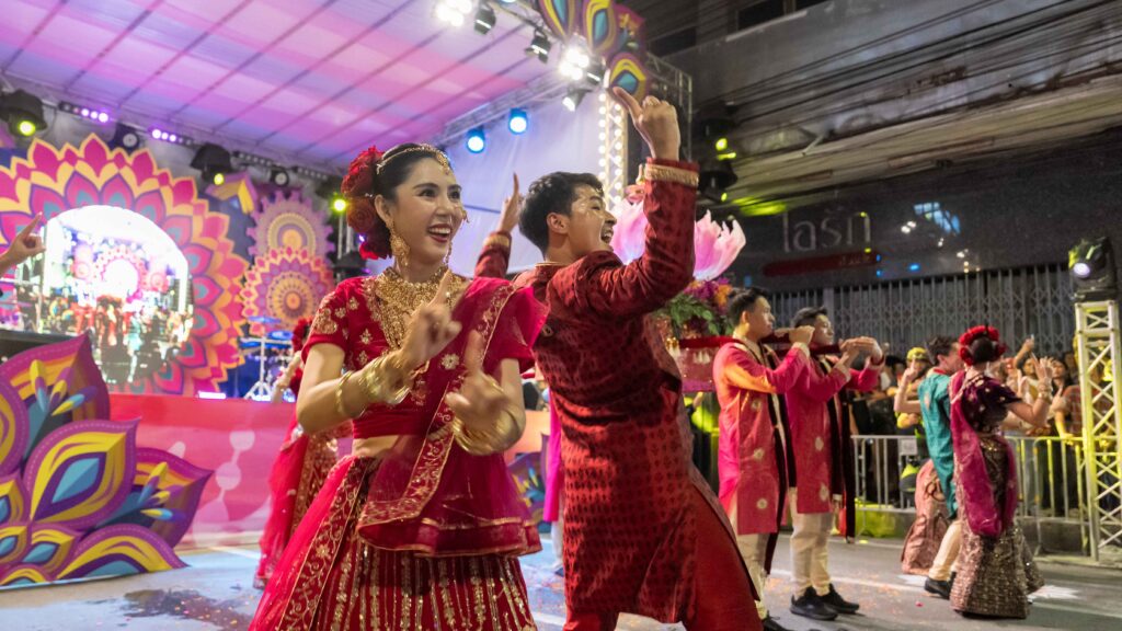 Performers in vibrant red and gold attire dance joyfully on stage at the Amazing Thailand Grand Diwali Festival 2025, celebrating Thai–Indian friendship.