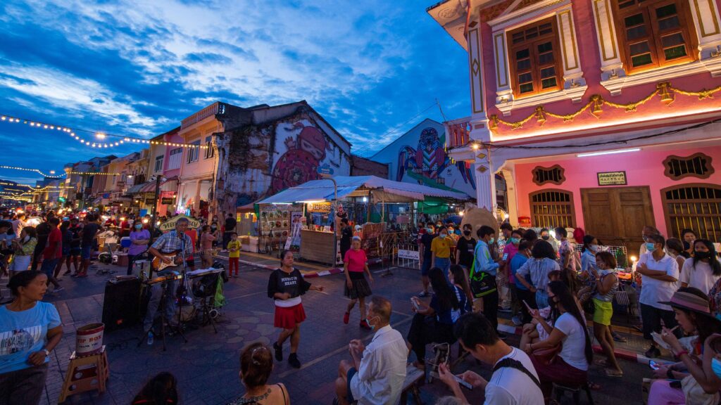 Tourists exploring Phuket’s lively Lard Yai Walking Street filled with street food, music, and colourful Sino-Portuguese buildings.