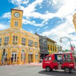 Vibrant yellow Sino-Portuguese buildings and red songthaew in Phuket Old Town under a bright blue sky.