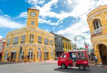 Vibrant yellow Sino-Portuguese buildings and red songthaew in Phuket Old Town under a bright blue sky.