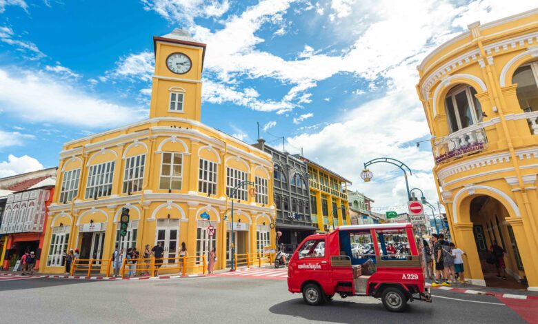 Vibrant yellow Sino-Portuguese buildings and red songthaew in Phuket Old Town under a bright blue sky.