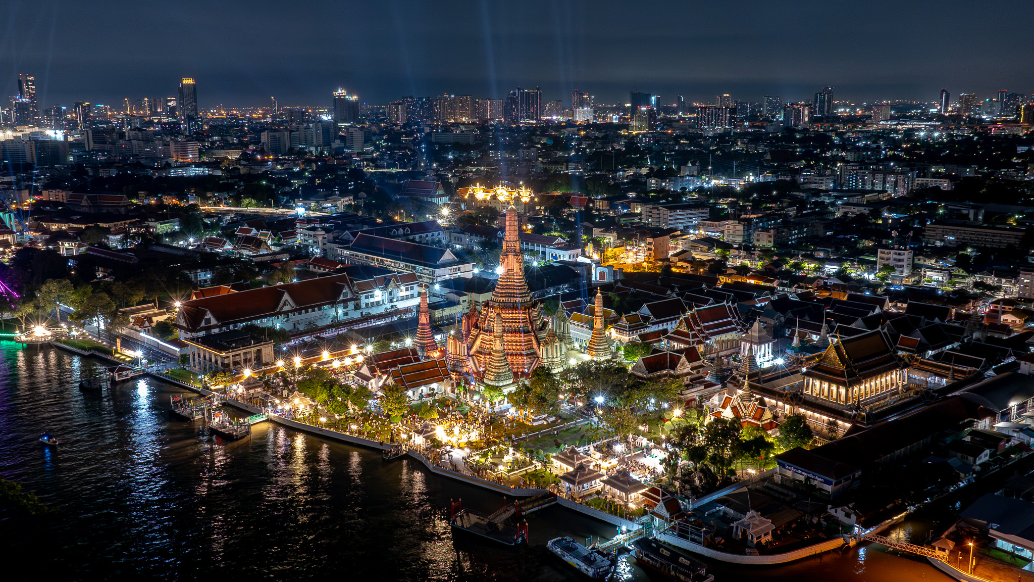 Aerial view of Wat Arun and the Chao Phraya River beautifully lit during a nighttime festival in Bangkok.