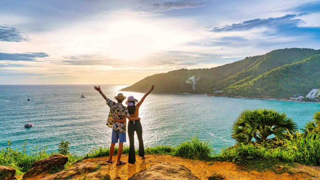 Couple admiring the sunset from Windmill Viewpoint overlooking Ya Nui Beach and the Andaman Sea in Phuket.