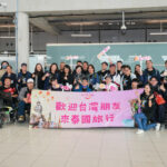 A large Taiwanese accessible tourism group poses with TAT representatives at Suvarnabhumi Airport, holding a welcome banner and “Amazing Thailand” signs.