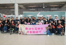 A large Taiwanese accessible tourism group poses with TAT representatives at Suvarnabhumi Airport, holding a welcome banner and “Amazing Thailand” signs.