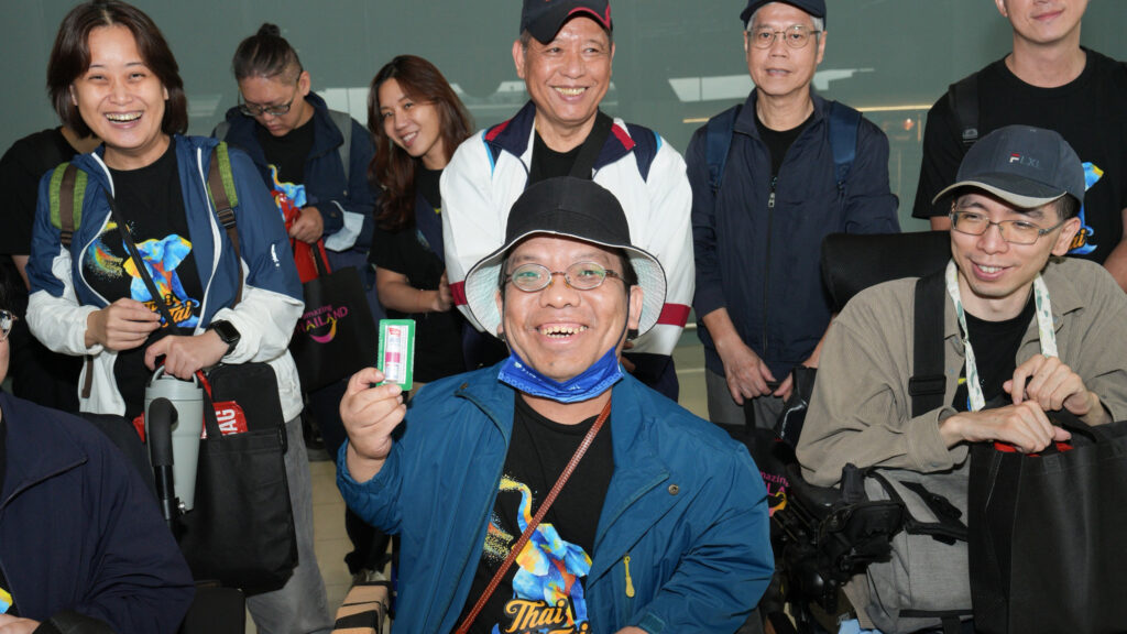 Taiwanese travellers, including participants using wheelchairs, smile and show souvenirs received during the welcome event at Suvarnabhumi Airport.