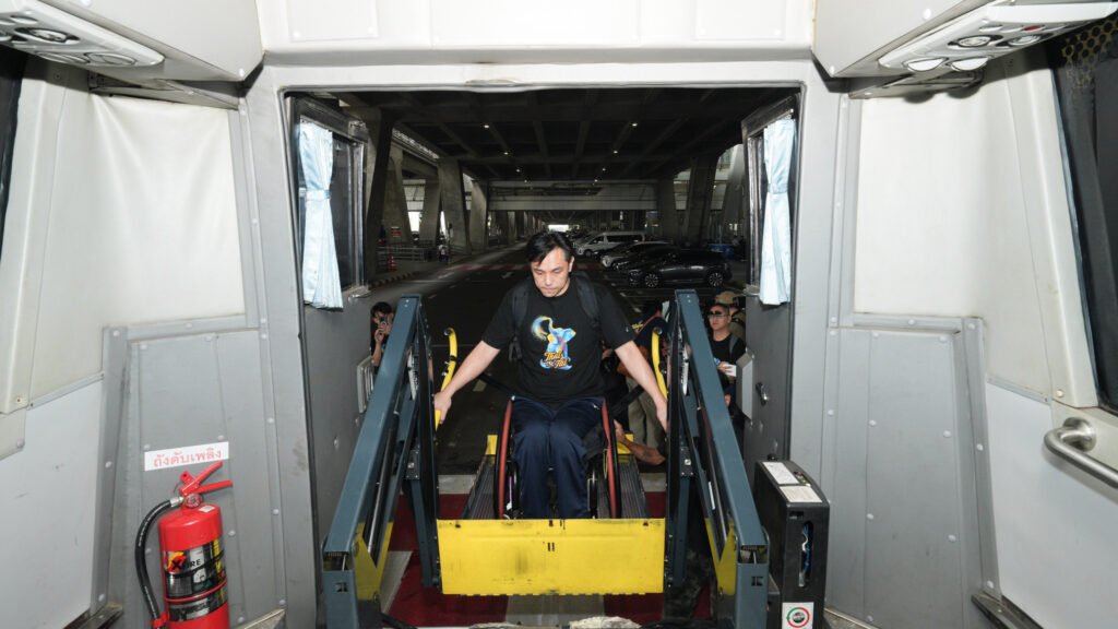A traveller using a wheelchair descends on an airport wheelchair lift vehicle at Suvarnabhumi Airport, demonstrating accessible arrival support.