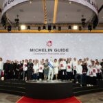 A large group of chefs and representatives stand on stage during the MICHELIN Guide Ceremony Thailand 2026, celebrating new award recipients.