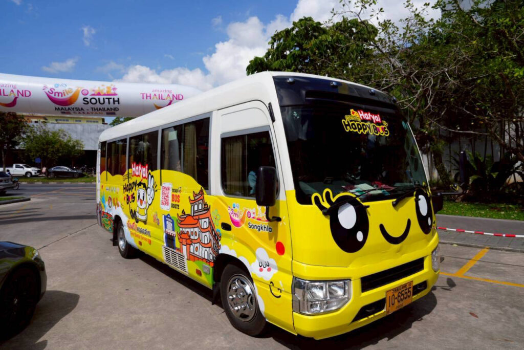 The Amazing Hatyai Happy Bus parked in Hat Yai city, showcasing the bright yellow Smile@Hatyai design promoting free shuttle services.
