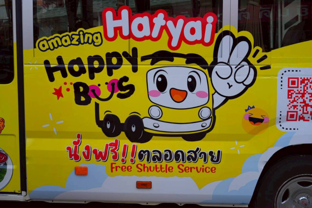 Close-up of the Amazing Hatyai Happy Bus exterior featuring the cartoon bus mascot and “Free Shuttle Service” signage.