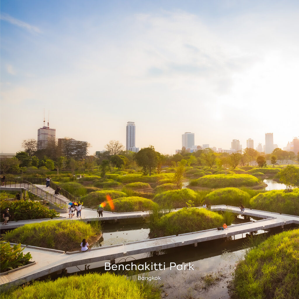 Sunset over Benchakiti Park’s rewilded wetlands with elevated walkways, grassy mounds and Bangkok’s skyline in the distance.