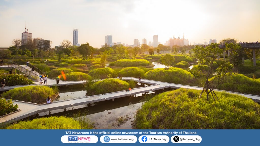 Sunset view of Benjakitti Park’s wetlands in Bangkok, with elevated walkways, lush green mounds, and the city skyline in the background.
