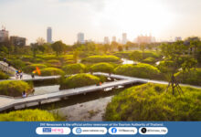 Sunset view of Benjakitti Park’s wetlands in Bangkok, with elevated walkways, lush green mounds, and the city skyline in the background.