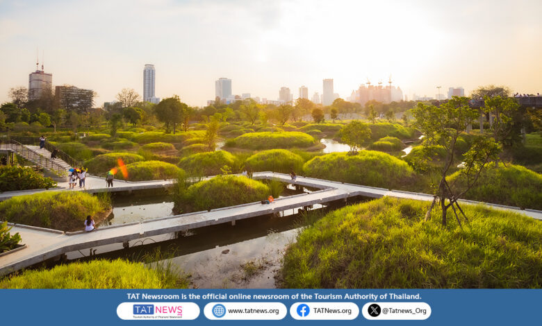 Sunset view of Benjakitti Park’s wetlands in Bangkok, with elevated walkways, lush green mounds, and the city skyline in the background.