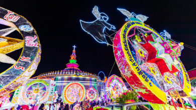 Illuminated star floats parade past the Cathedral of St Michael the Archangel during the Sakon Nakhon Christmas Star Parade, with angel motifs and vibrant lights lighting up the night sky.
