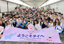 A large group of youth football players from Japan hold a “Welcome to Thailand” banner as TAT staff greet them on arrival in Bangkok.