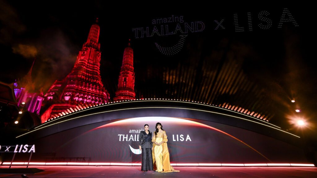 TAT unveils Lalisa LISA Manobal as Amazing Thailand Ambassador during a night-time launch at Wat Arun, Bangkok, featuring TAT Governor Ms. Thapanee Kiatphaibool alongside Lalisa ‘LISA’ Manobal on stage beneath the illuminated “Amazing Thailand x LISA” backdrop, with Wat Arun’s red-lit spires and a choreographed drone display lighting the night sky.