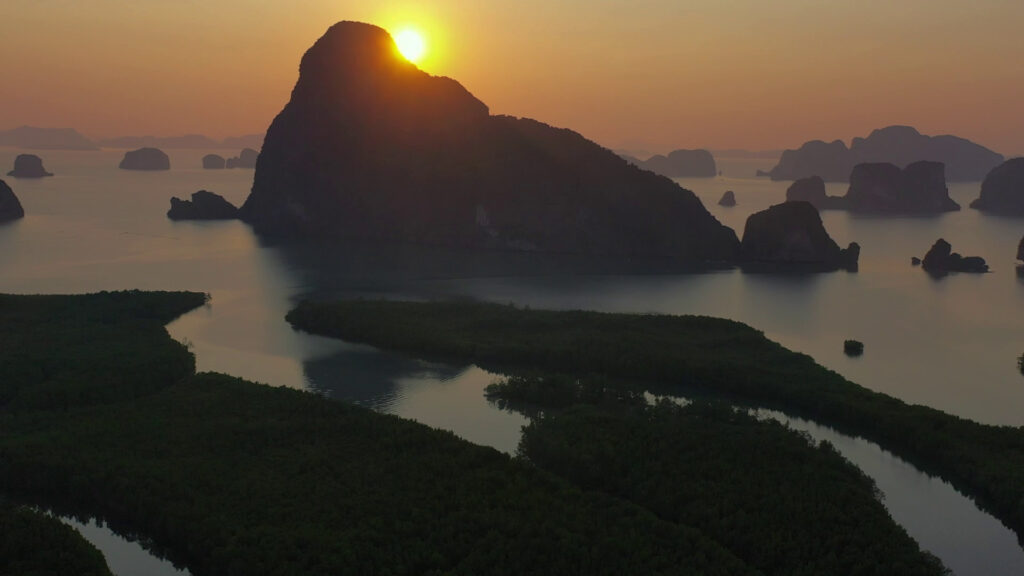 Sunrise behind a limestone karst and islands over calm southern seas and mangroves