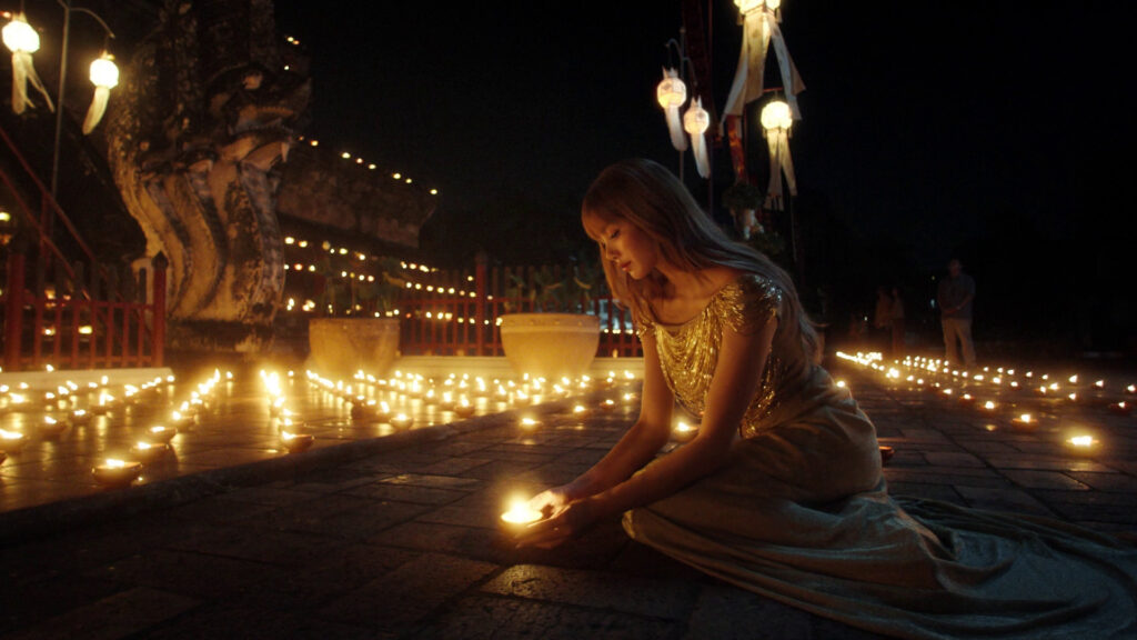 Lalisa “LISA” Manobal lighting a candle on a temple courtyard at night