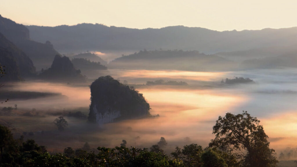 Sunrise over a mist-filled valley with rock outcrops and layered hills