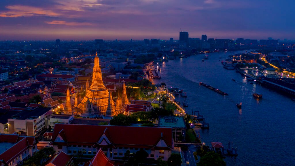 Aerial night view of Wat Arun illuminated along the Chao Phraya River in Bangkok, highlighting Thailand’s position as a top global holiday destination for 2026.