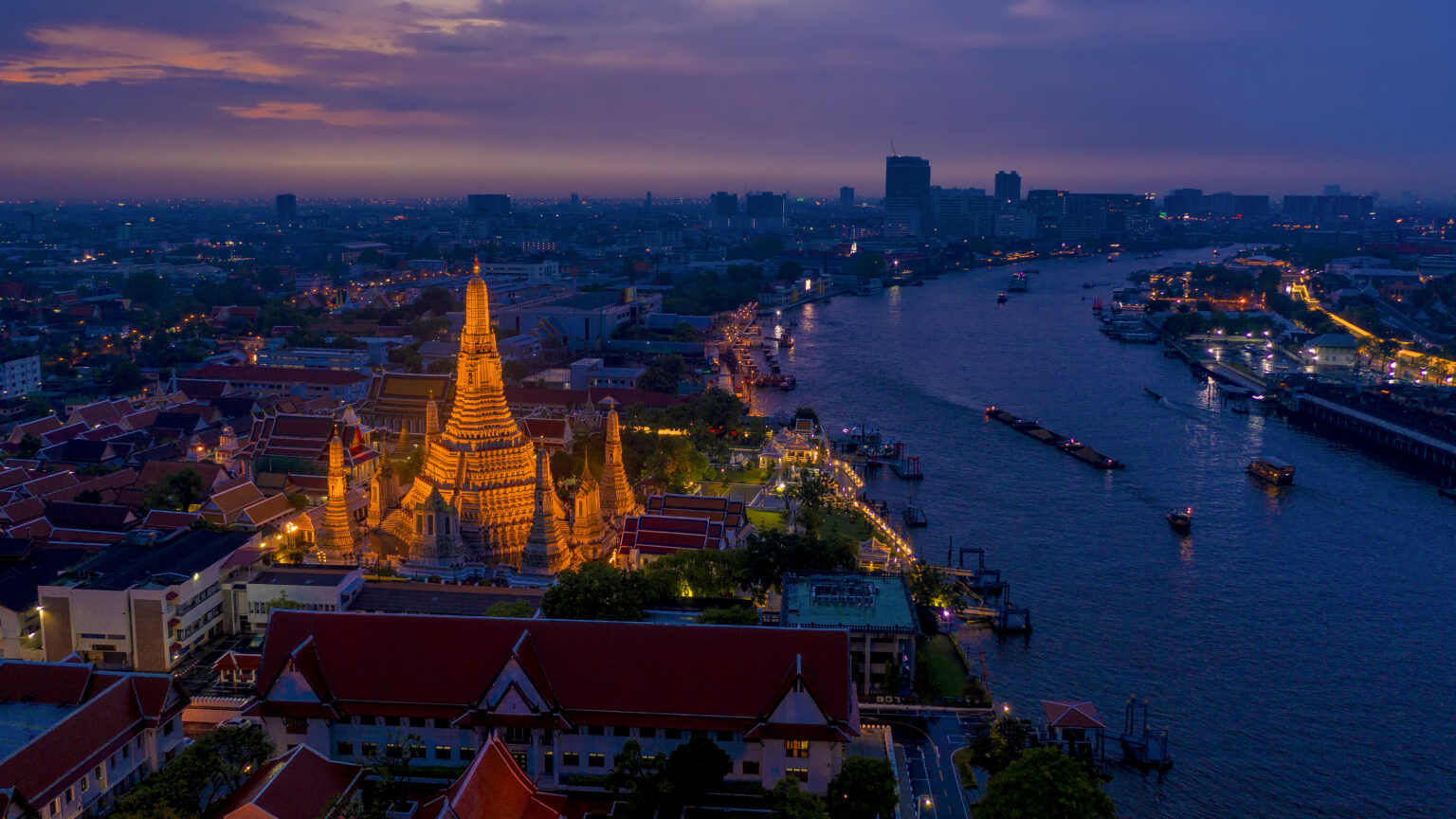 Aerial night view of Wat Arun illuminated along the Chao Phraya River in Bangkok, highlighting Thailand’s position as a top global holiday destination for 2026.