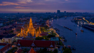 Aerial night view of Wat Arun illuminated along the Chao Phraya River in Bangkok, highlighting Thailand’s position as a top global holiday destination for 2026.