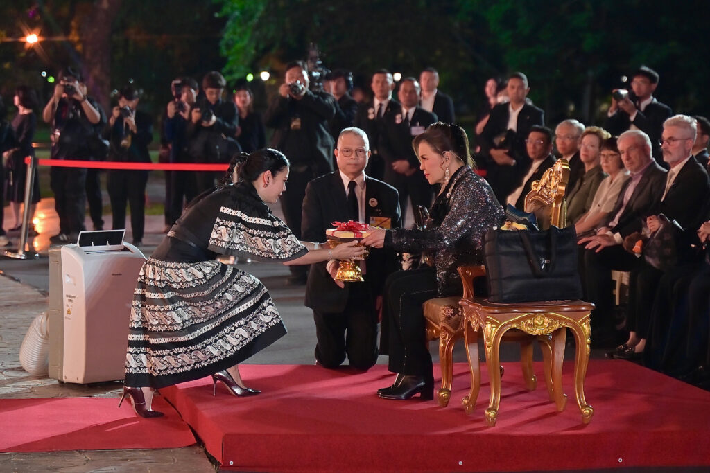 A ceremonial moment captures HRH Princess Ubolratana receiving a presentation from TAT Governor Thapanee Kiatphaibool during the opening programme, observed by senior officials and an audience seated in the background.