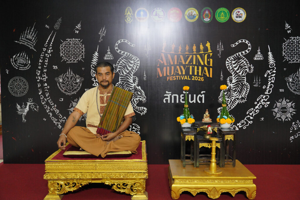 A Muay Thai master sits in a traditional setting with ceremonial elements and yantra designs as part of the cultural display for Amazing MuayThai Festival 2026.
