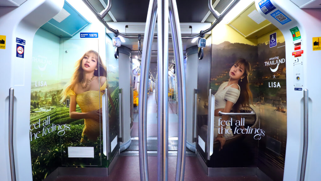 Interior of BTS Skytrain wrapped with Amazing Thailand x LISA campaign visuals featuring Chiang Rai tea plantations and riverside night scenery.