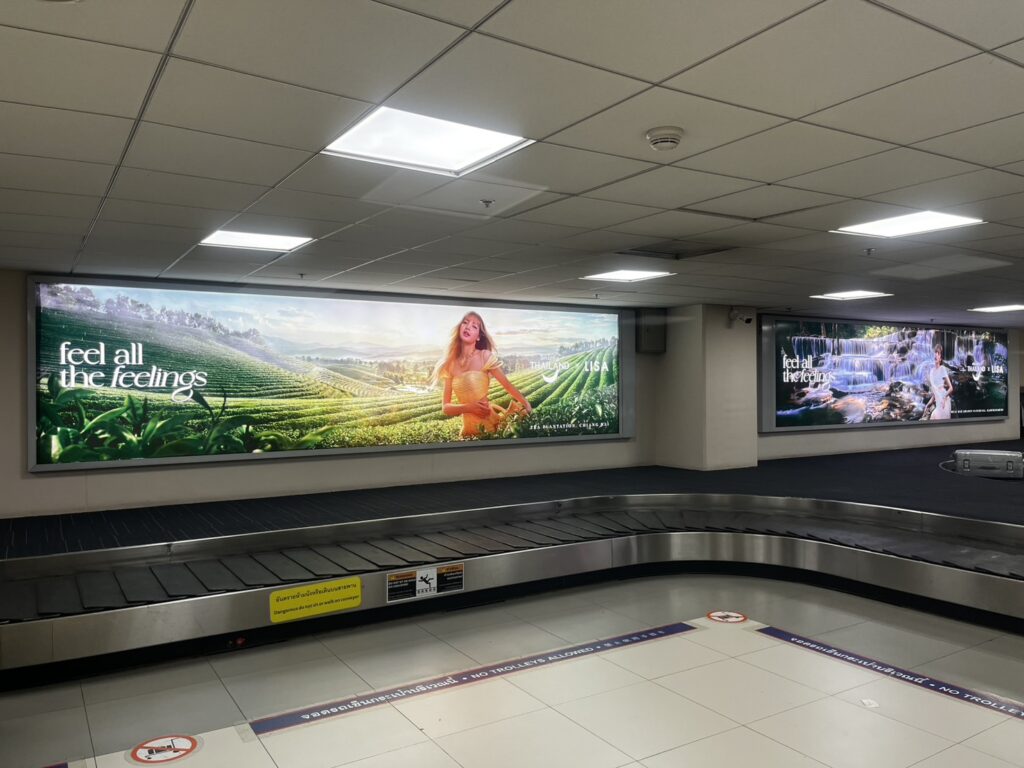 Amazing Thailand x LISA campaign displays at Don Mueang International Airport baggage claim showcasing Chiang Rai tea plantations and waterfall scenery.