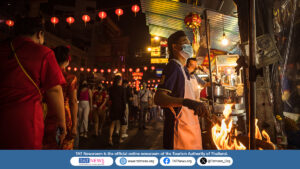 Street food vendor cooking over open flame in Yaowarat, Bangkok, under red Chinese lanterns, reflecting Chinese influence on Thai cuisine and vibrant night market culture.