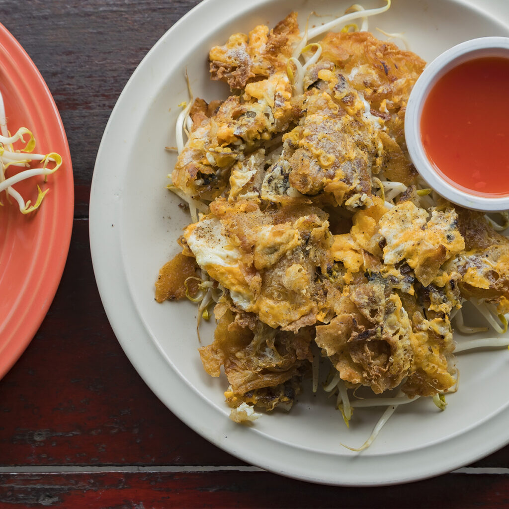 Hoi Tod crispy oyster omelet served with sweet chili sauce, showcasing Chinese cooking techniques adapted into Thai street food.