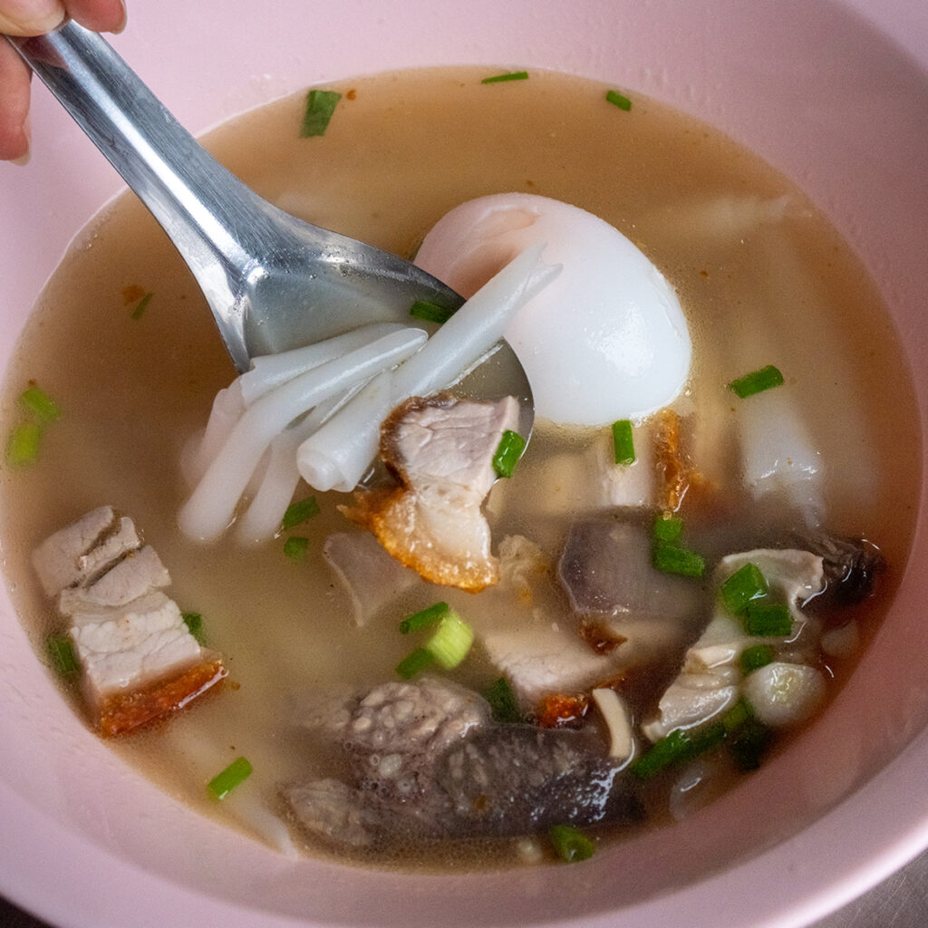 Kuay Jab rolled rice noodle soup with crispy pork and peppery broth, highlighting Chinese influence on Thai cuisine in Bangkok’s street food scene.