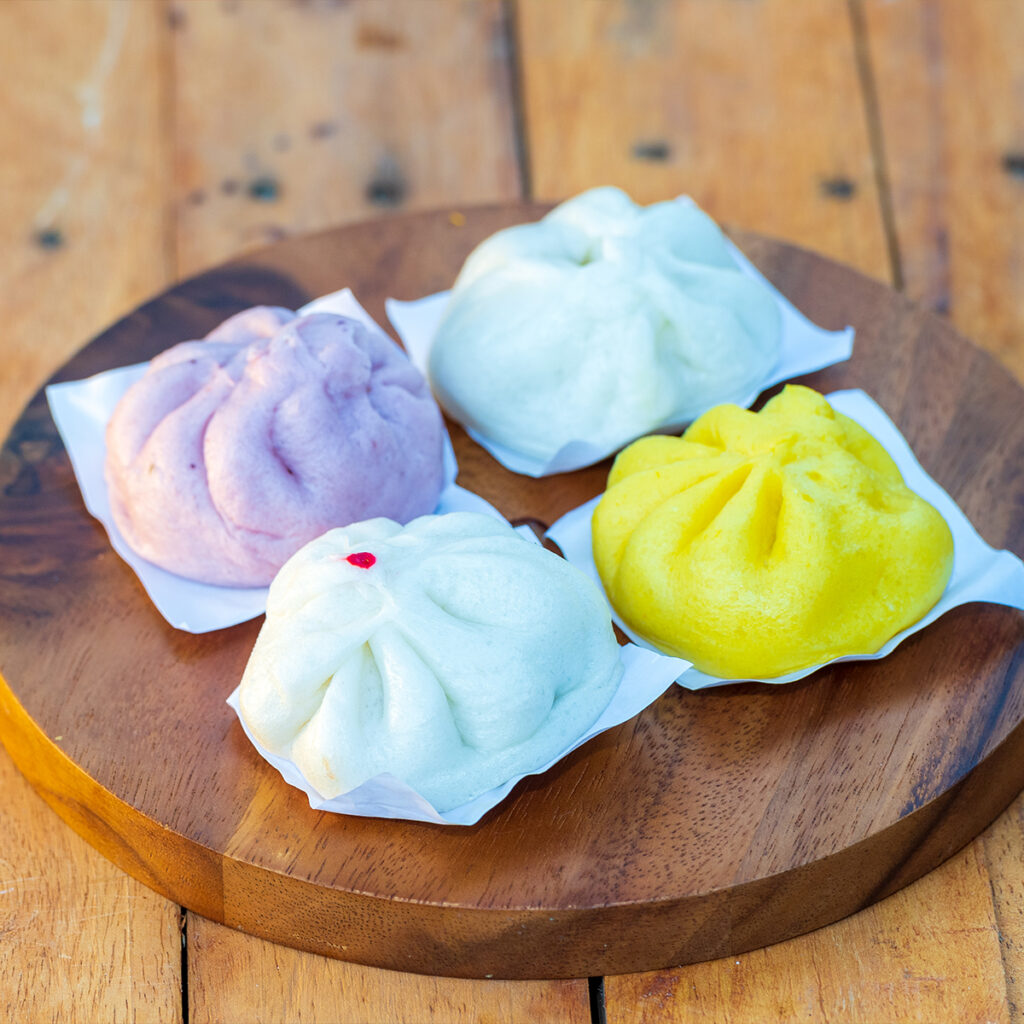 Colorful Salapao steamed buns on wooden tray, reflecting Chinese culinary roots in Thai street food culture.