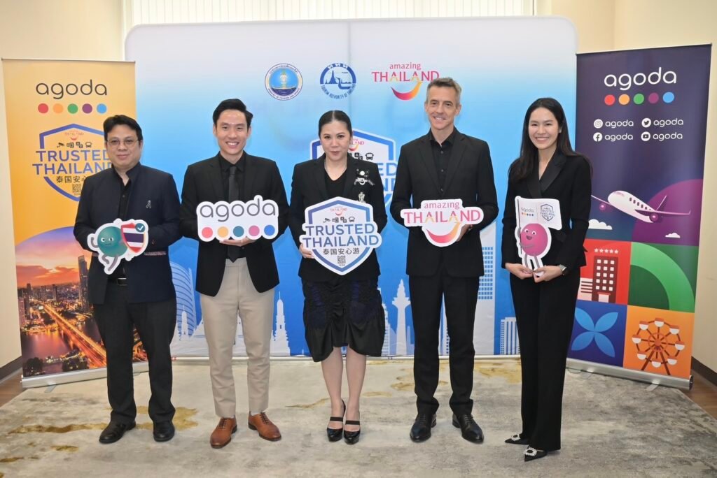 Group photo of representatives from the Tourism Authority of Thailand and Agoda standing before Trusted Thailand and Amazing Thailand backdrops, holding campaign signage during the partnership meeting in Bangkok.