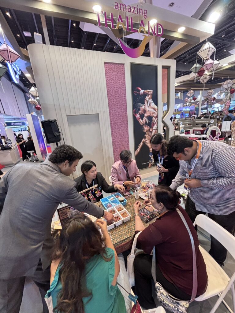 Visitors taking part in a Thai cultural craft demonstration at the Thailand pavilion during Outbound Travel Mart 2026, interacting with traditional materials and hands-on activities.