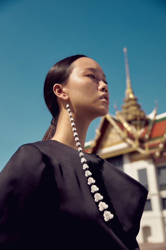 Close-up of SARRAN The Ambassador Collection jasmine-inspired statement earrings against a Thai temple backdrop.