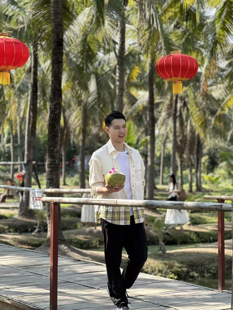 Chinese TV host enjoying fresh coconut drink beneath lanterns in northern Thailand cultural setting.