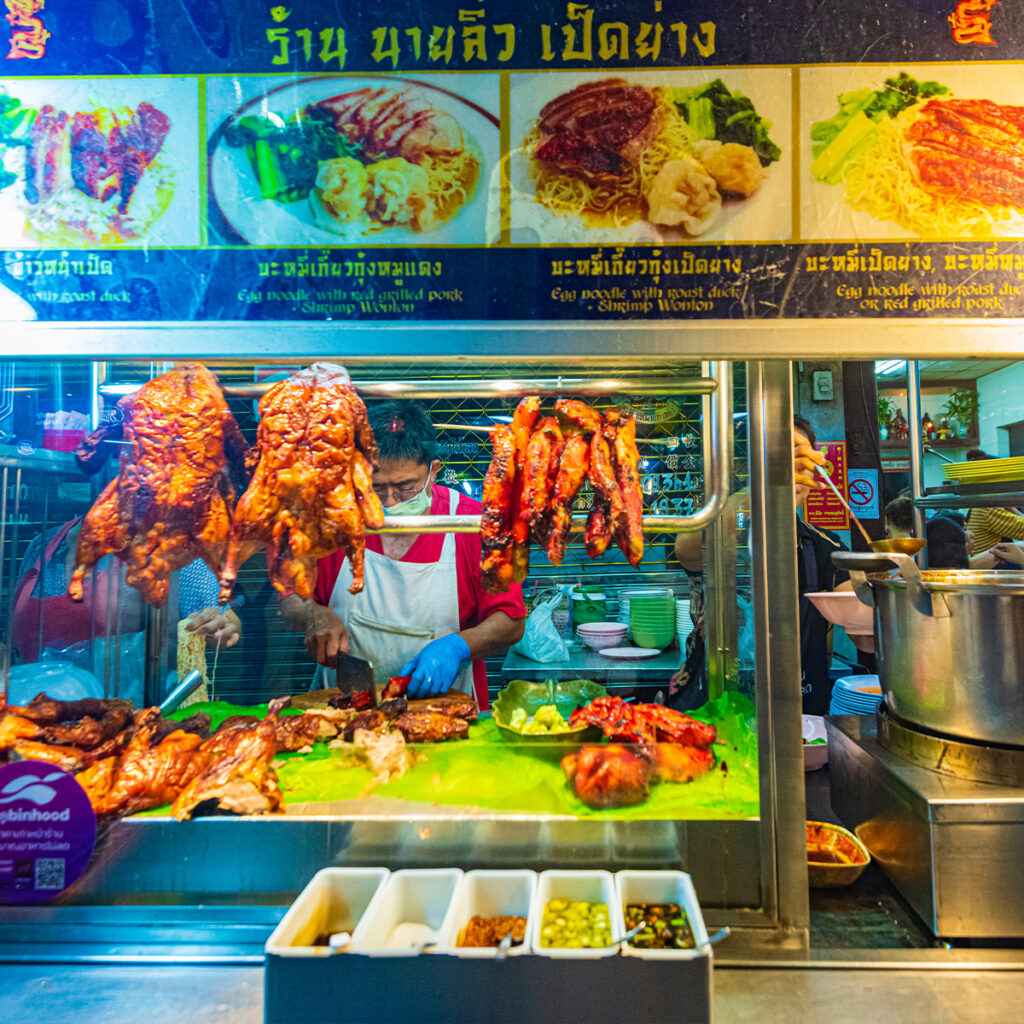 Roast duck and red pork hanging at Yaowarat food stall in Bangkok, reflecting Chinese culinary heritage in Thai street food culture.
