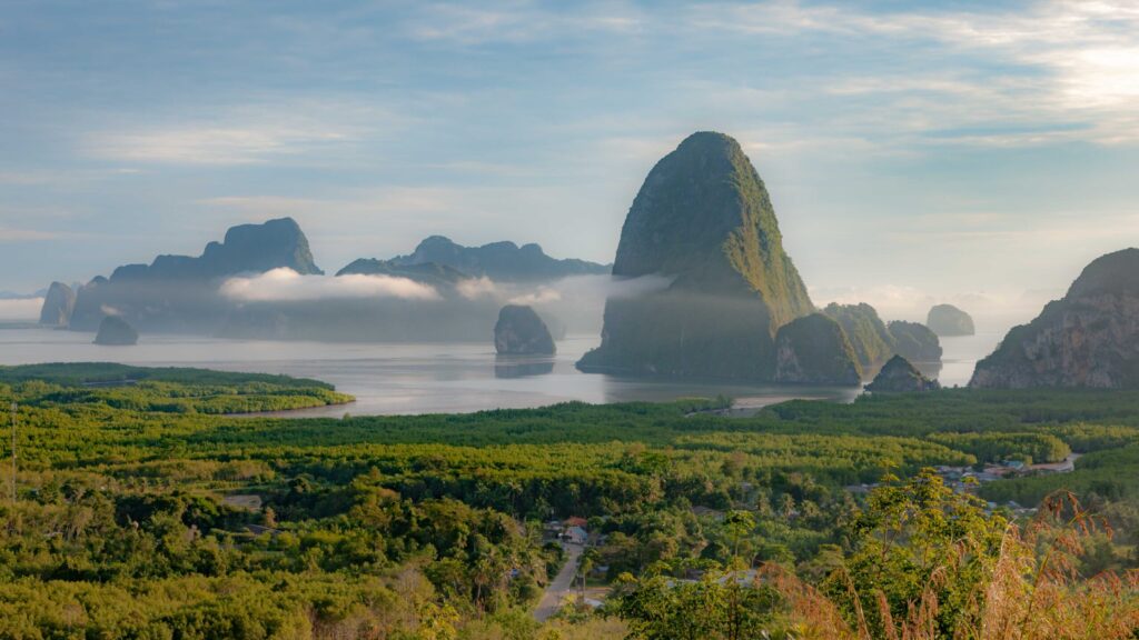 Morning mist drifts across limestone karsts and lush mangroves at Ao To Li Viewpoint, Phang-nga, during Thailand’s green season.