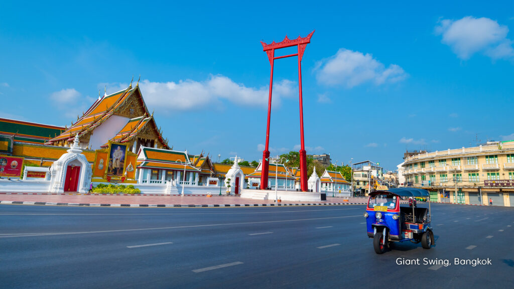 Bangkok’s Giant Swing beside Wat Suthat, with a colourful tuk-tuk travelling along the historic city street.