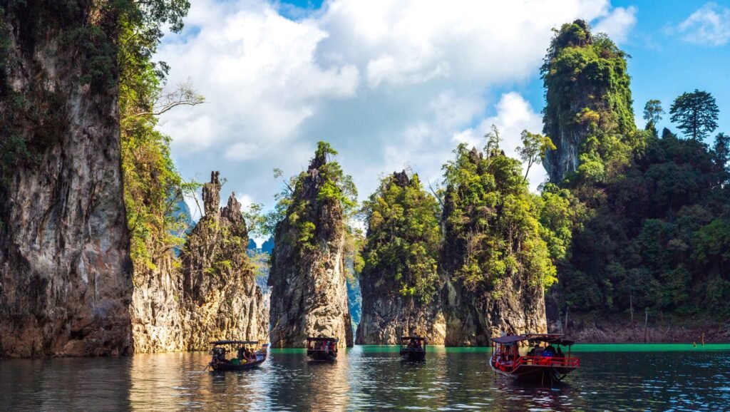 Long-tail boats cruise through limestone cliffs and emerald waters at Khao Sok National Park in Surat Thani, Thailand.