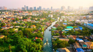 Aerial view of Sanam Chai Canal winding through a leafy Bangkok neighbourhood, with a long-tail boat travelling along the waterway.