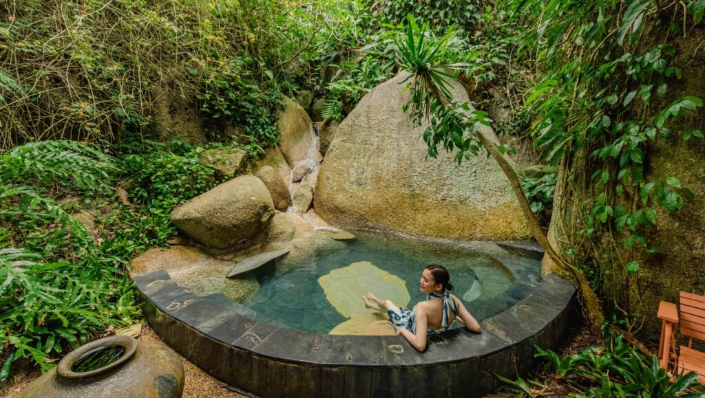 A visitor relaxes in a forest spa pool surrounded by tropical greenery at Tamarind Springs, Ko Samui.